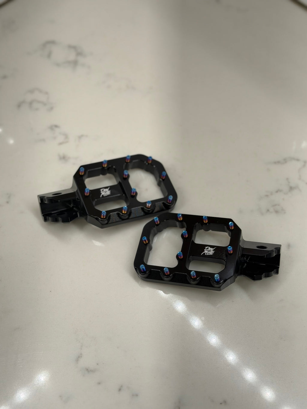 DevMoto E-Moto foot pegs for motorcycles, showing close-up of durable metal foot pegs with textured surface for grip.
