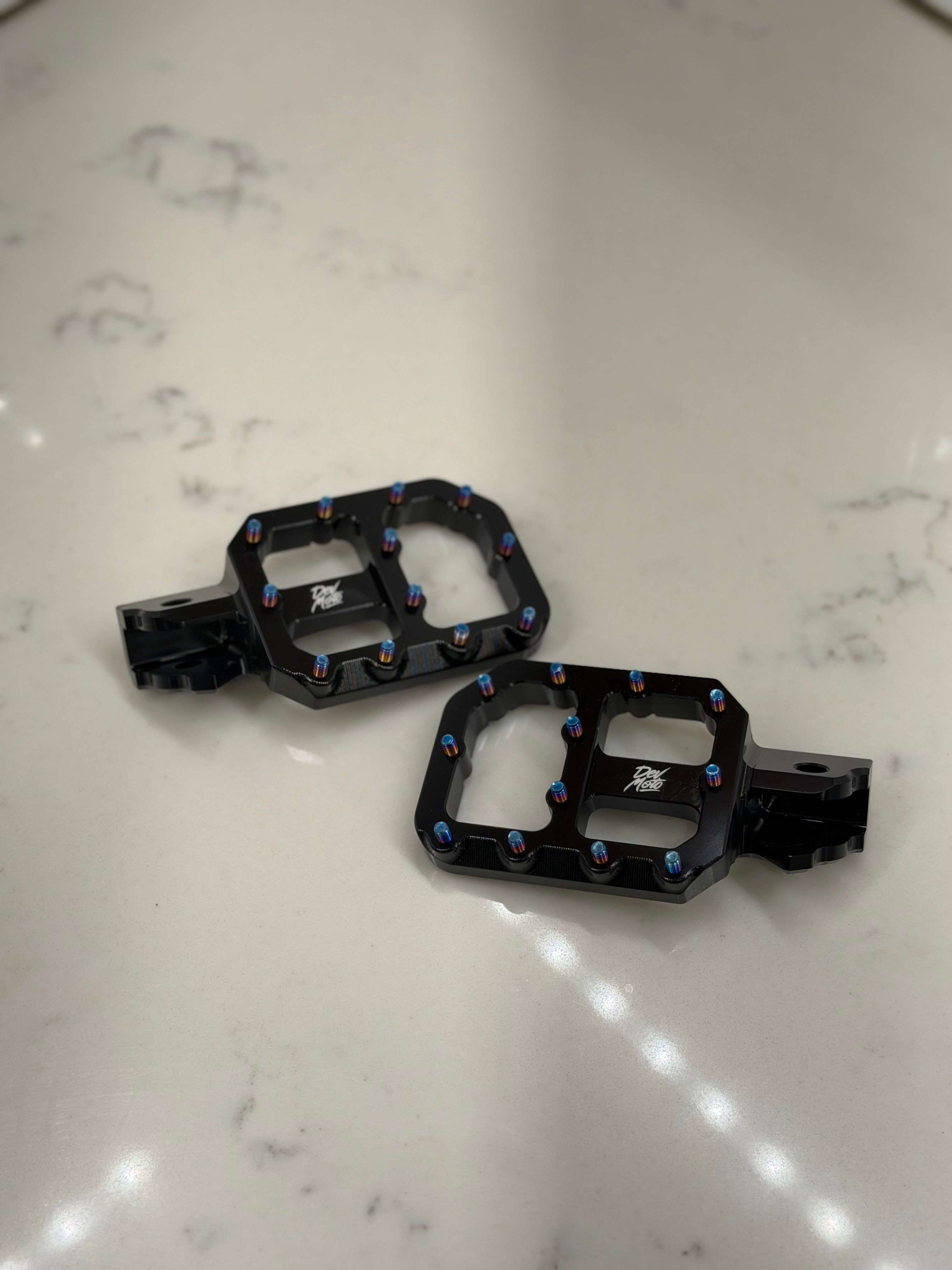 DevMoto E-Moto foot pegs for motorcycles, showing close-up of durable metal foot pegs with textured surface for grip.