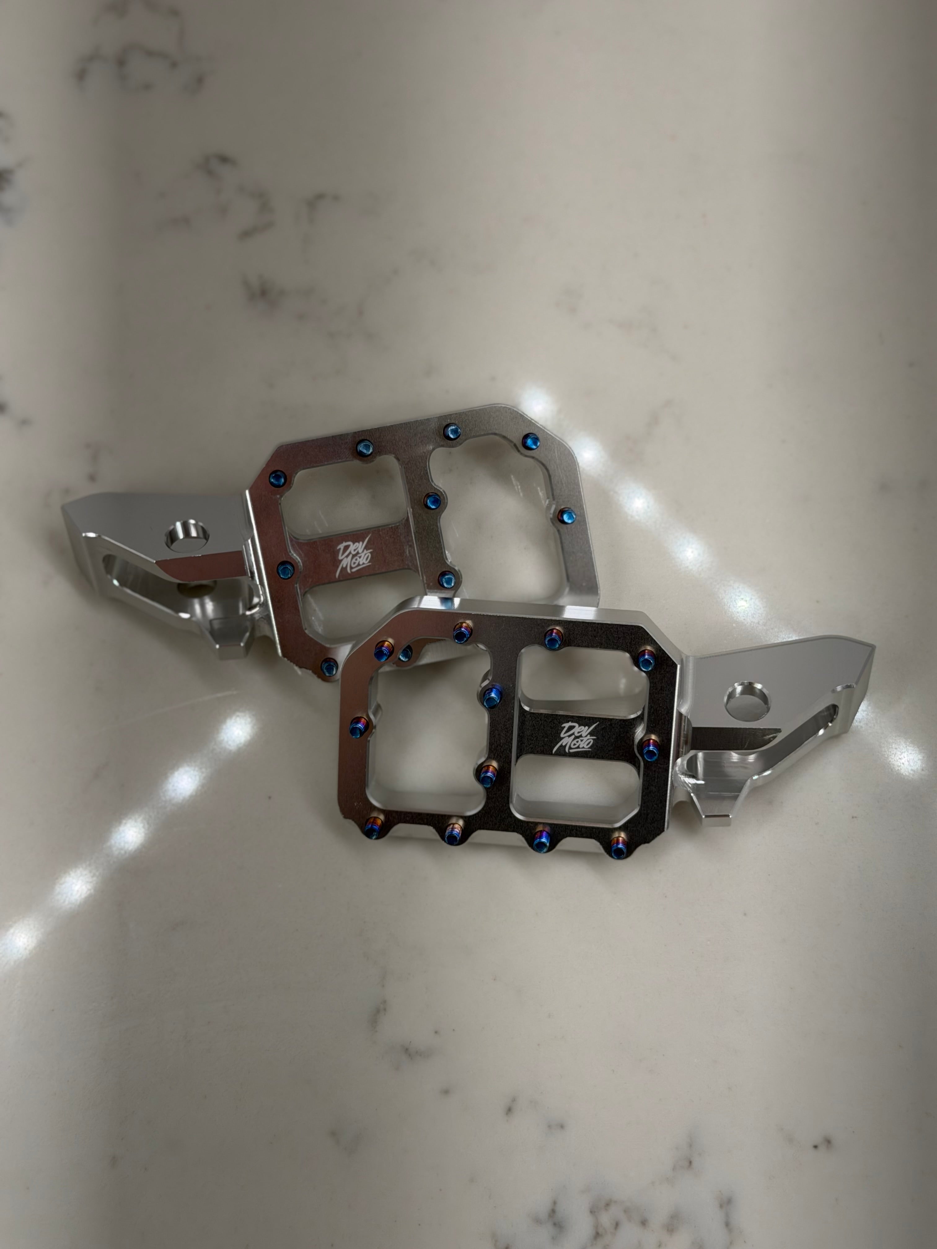 DevMoto E-Moto foot pegs for motorcycles, showing durable metal construction and mounting brackets for enhanced riding comfort.