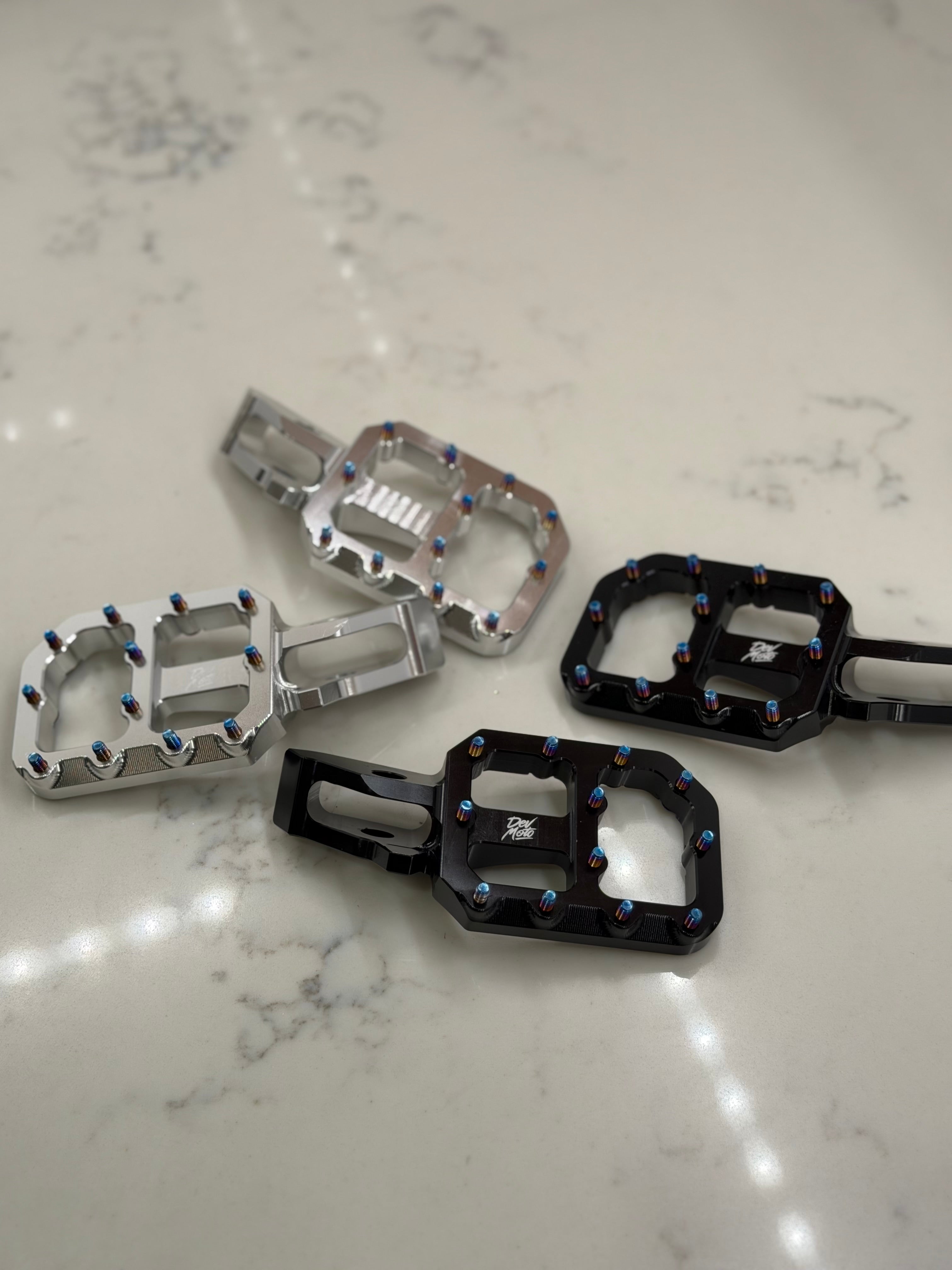 DevMoto E-Moto foot pegs mounted on motorcycle, durable metal footrests with textured surface for grip and stability.