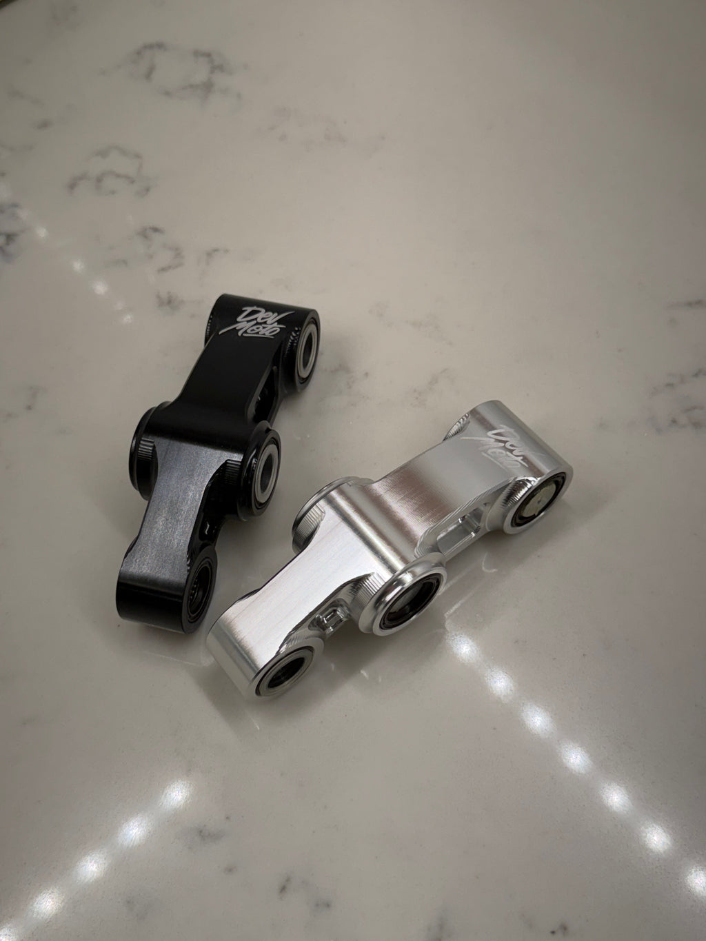 DevMoto E-Moto suspension linkage showing close-up of black metal component with mounting points and detailed craftsmanship.
