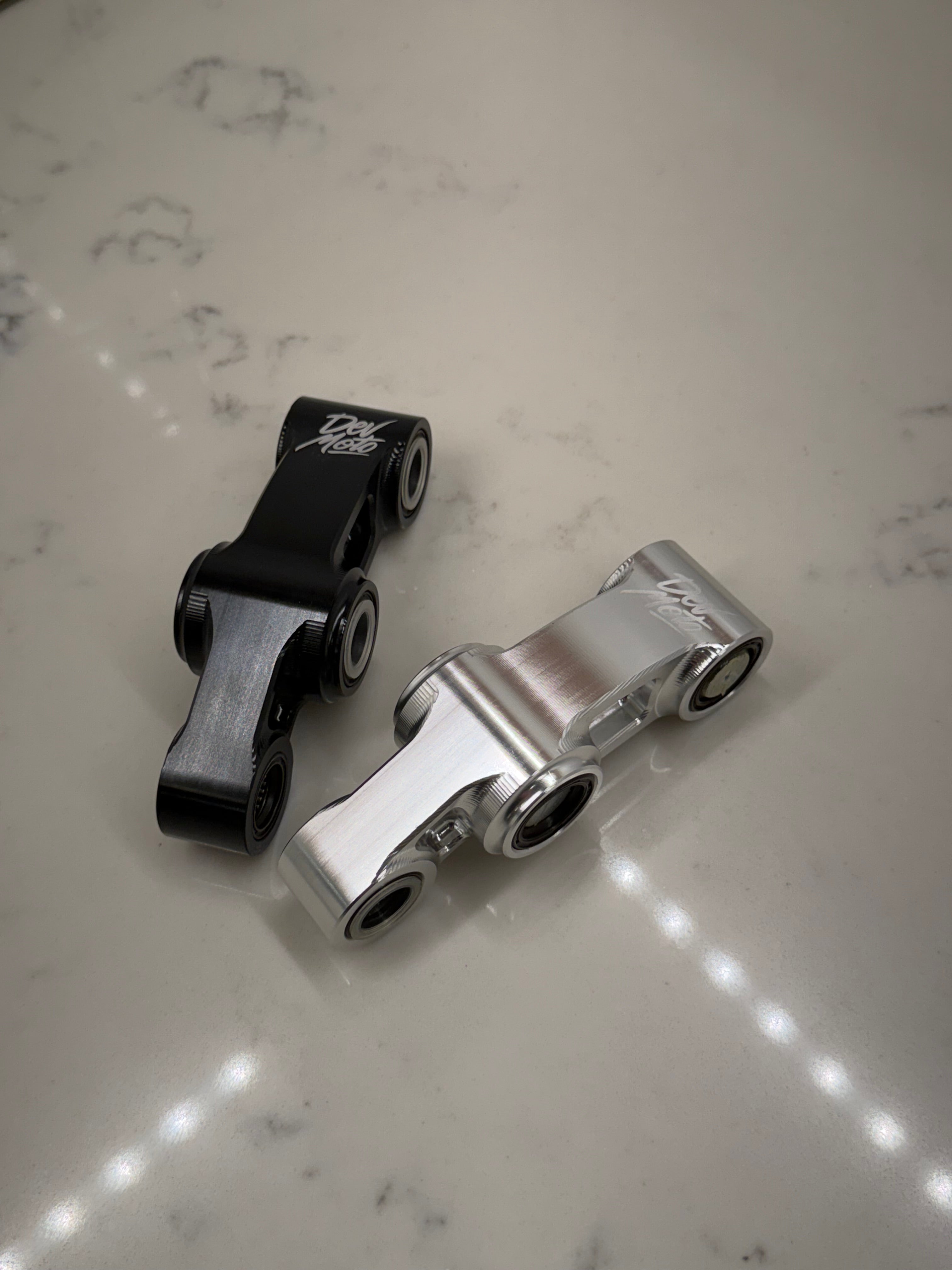 DevMoto E-Moto suspension linkage showing close-up of black metal component with mounting points and detailed craftsmanship.