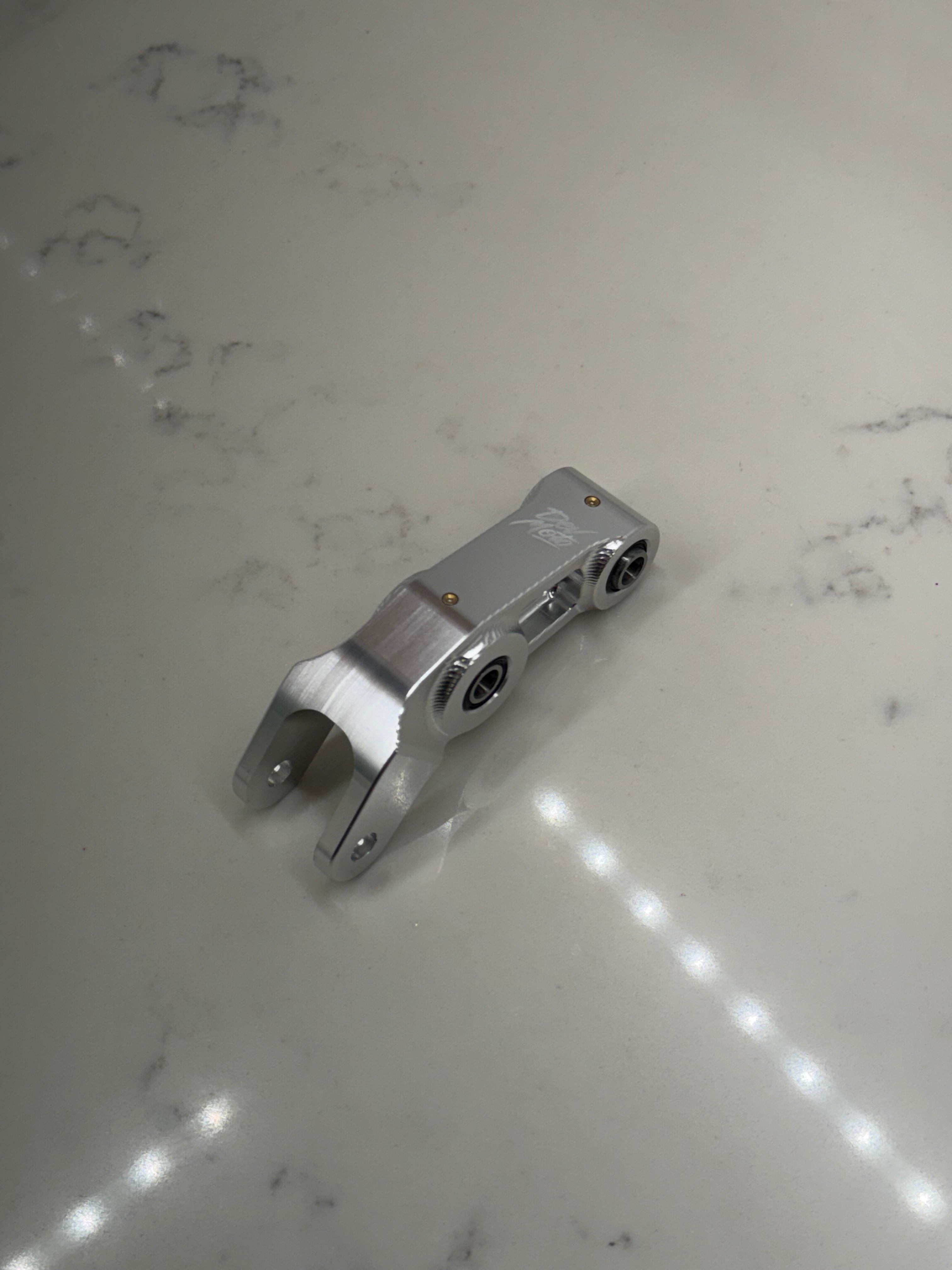 DevMoto E-Moto suspension linkage showing a close-up of the metal linkage component for electric motorcycle suspension system.