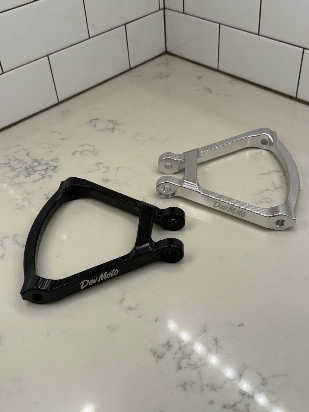 DevMoto E-Moto suspension triangle for electric motorcycle, showing the metal component with mounting points and sleek design.