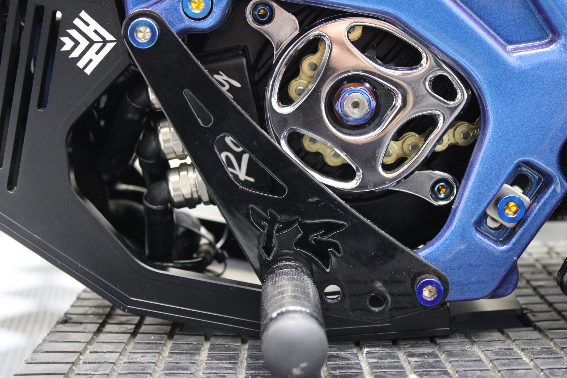 TG Racing Surron LBX Shiftlock bike part, showcasing the shiftlock mechanism with detailed metal components and branding.