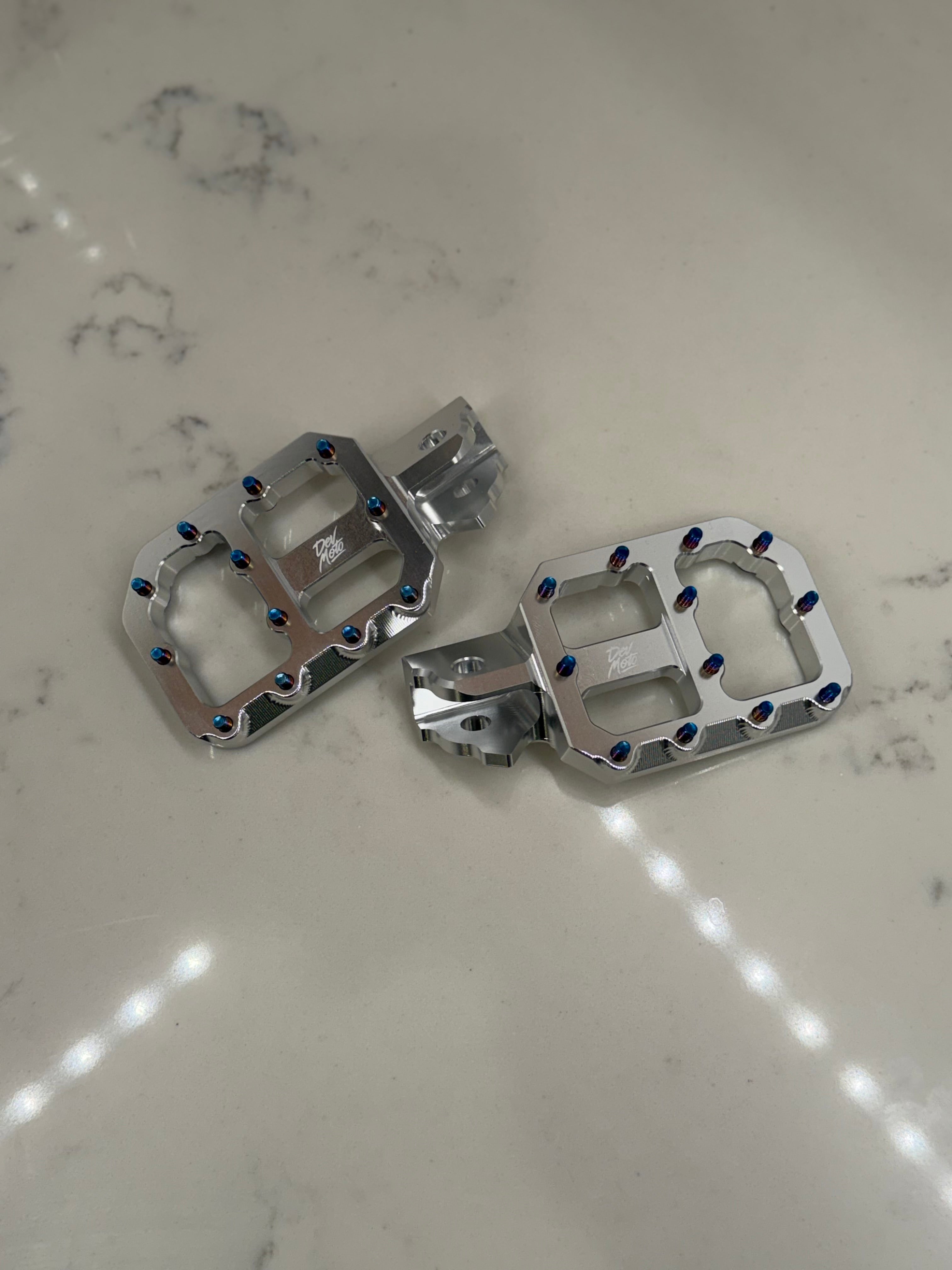 DevMoto E-Moto foot pegs designed for motorcycle riding, featuring durable metal construction with textured surfaces for grip.