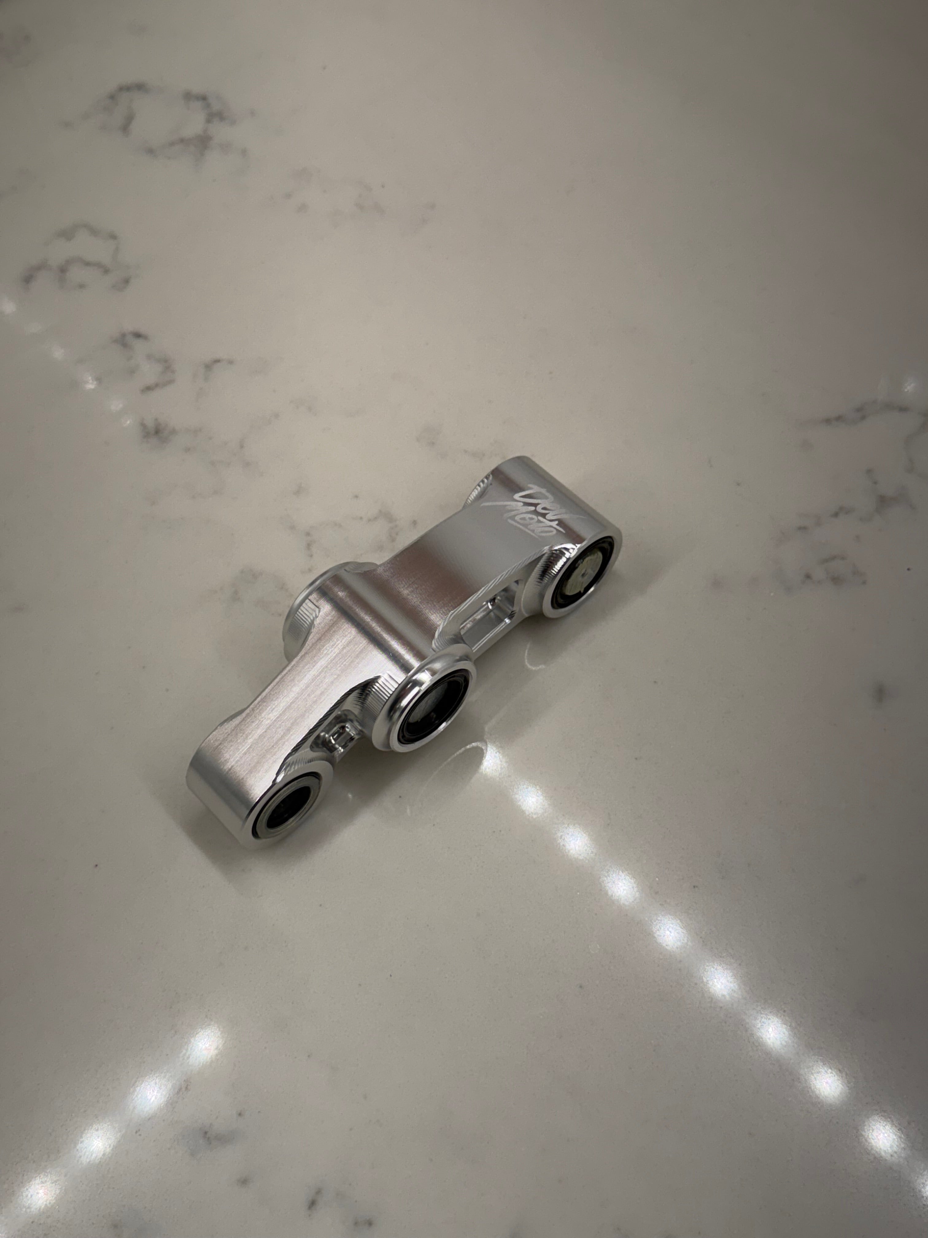 DevMoto E-Moto suspension linkage showing a close-up of the metal linkage part with mounting points.