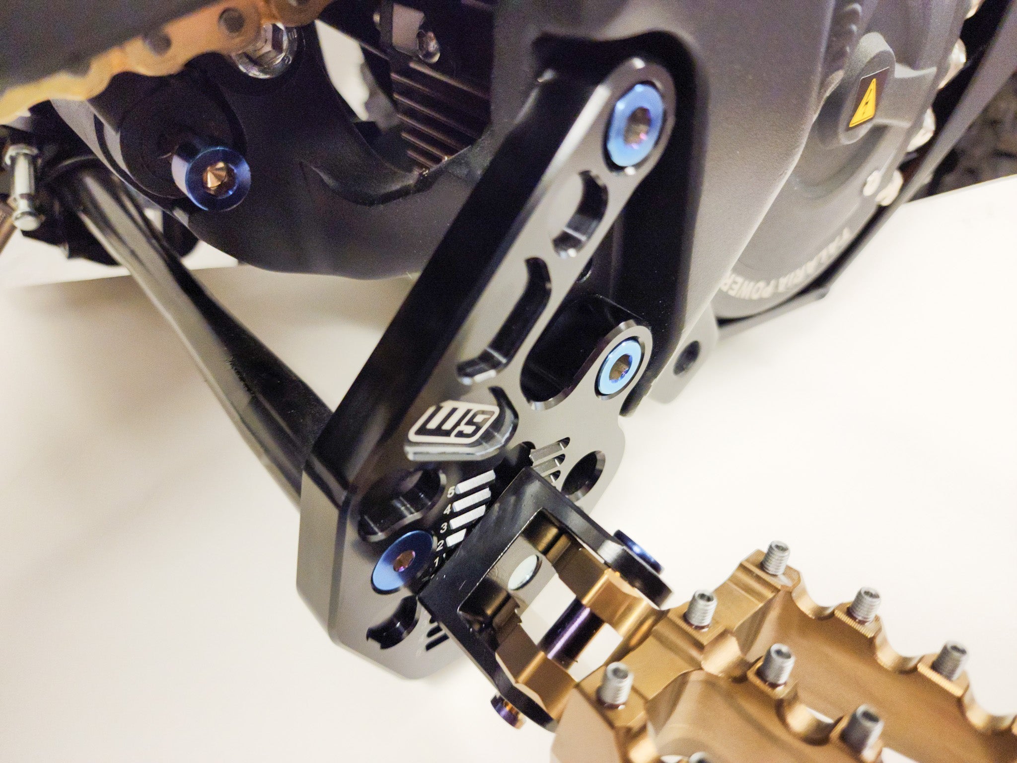 Modded Moto Co Warp 9 Talaria adjustable foot peg mount for motorcycle, showing the rugged metal construction and mounting bracket.