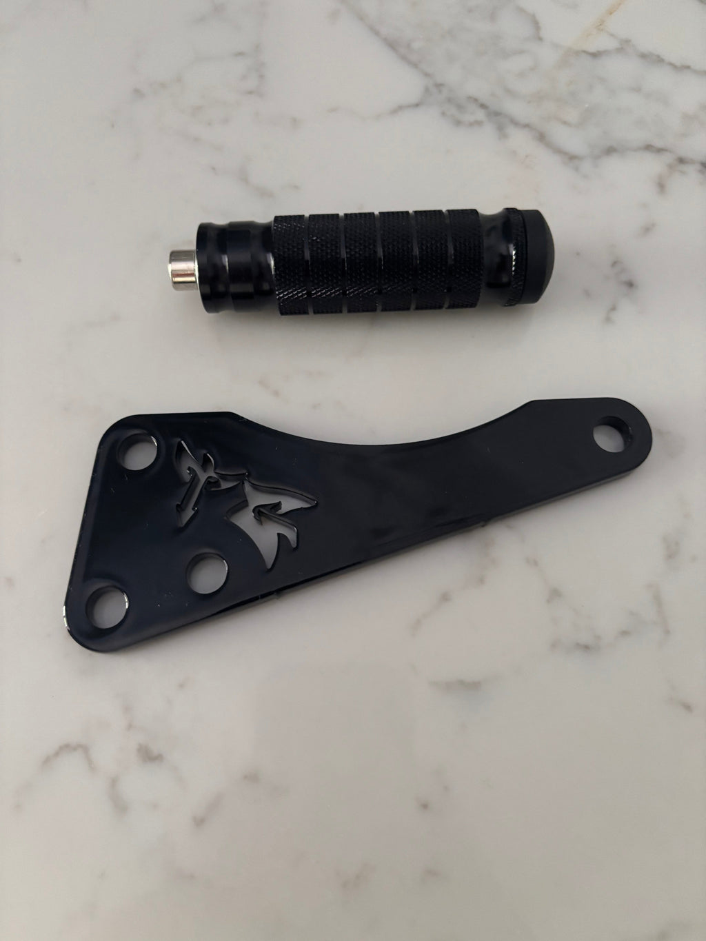 TG Racing Talaria X3 footlock and bracket, black metal components for bike security and stability, shown on a workbench.