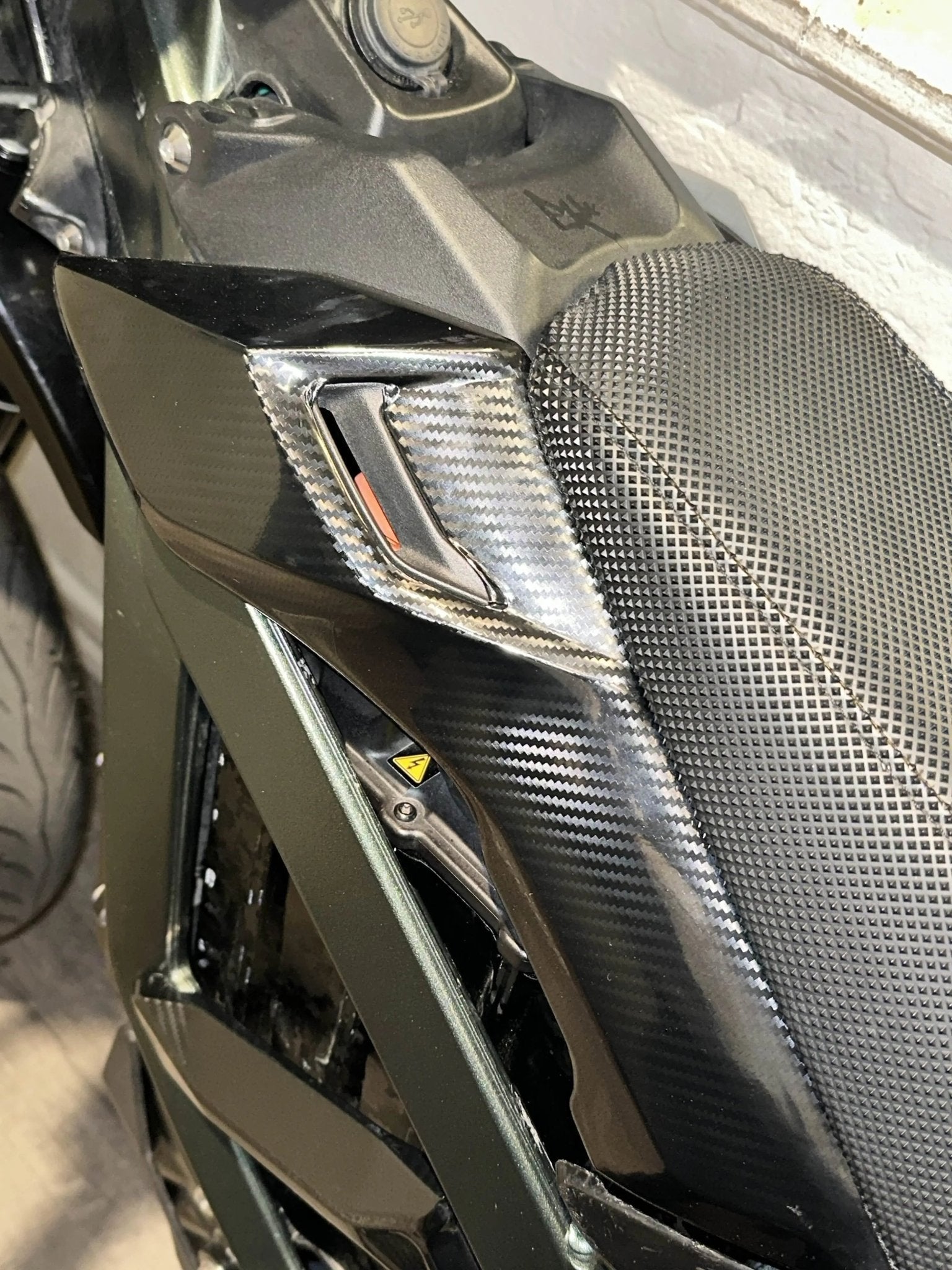 MXwraps Surron Ultra Bee carbon fiber vinyl wrap kit on battery lid sides, showcasing sleek black and textured carbon fiber finish.