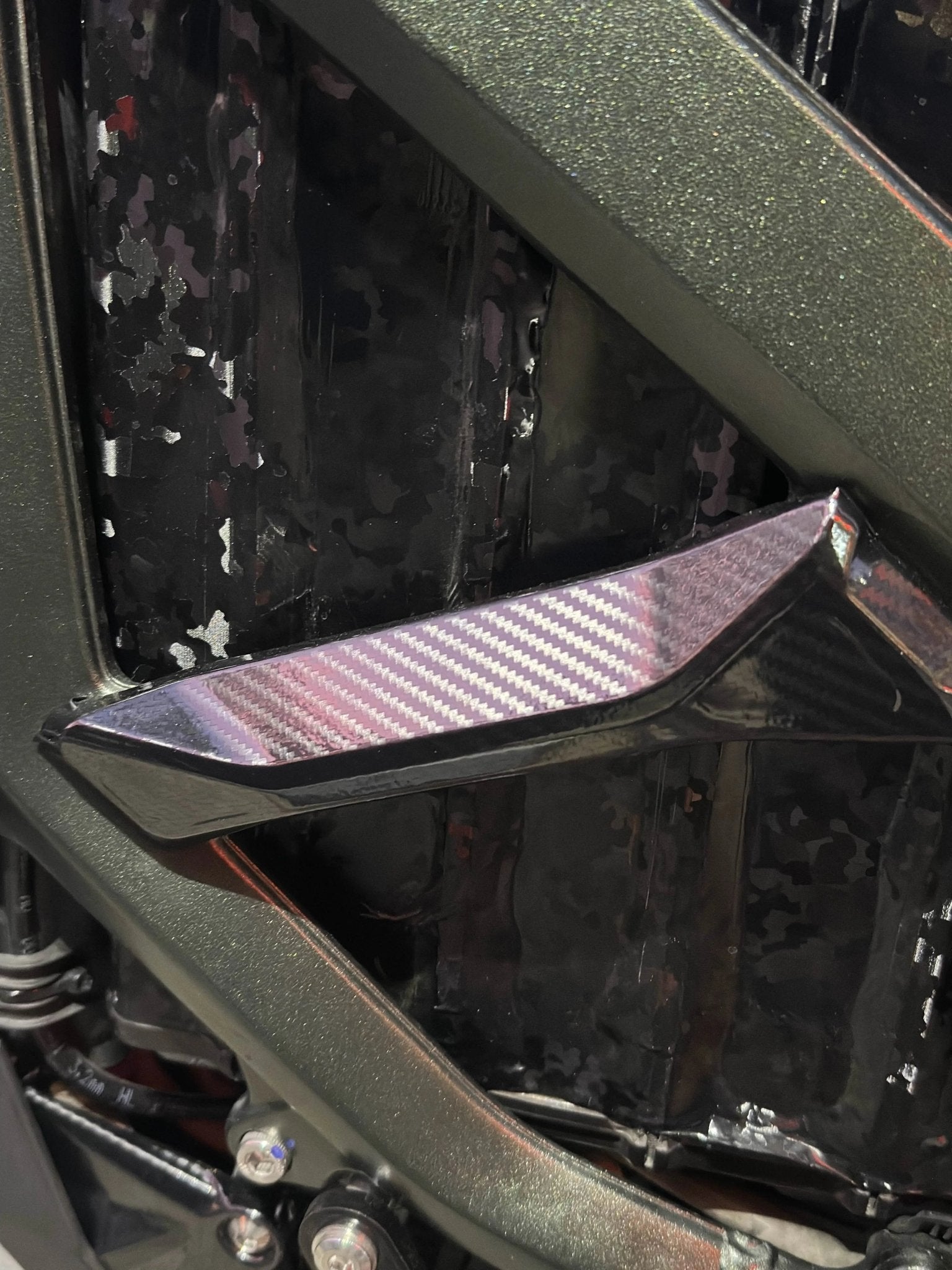 MXwraps Surron Ultra Bee carbon fiber vinyl wrap applied to side frames, showcasing sleek, textured finish on electric bike.