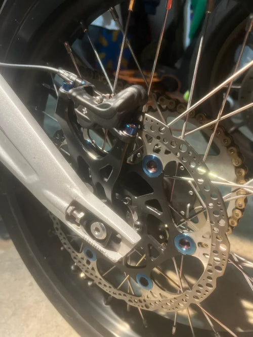 Titanium caliper bolts from DevMoto mounted on a motorcycle caliper for secure brake assembly.
