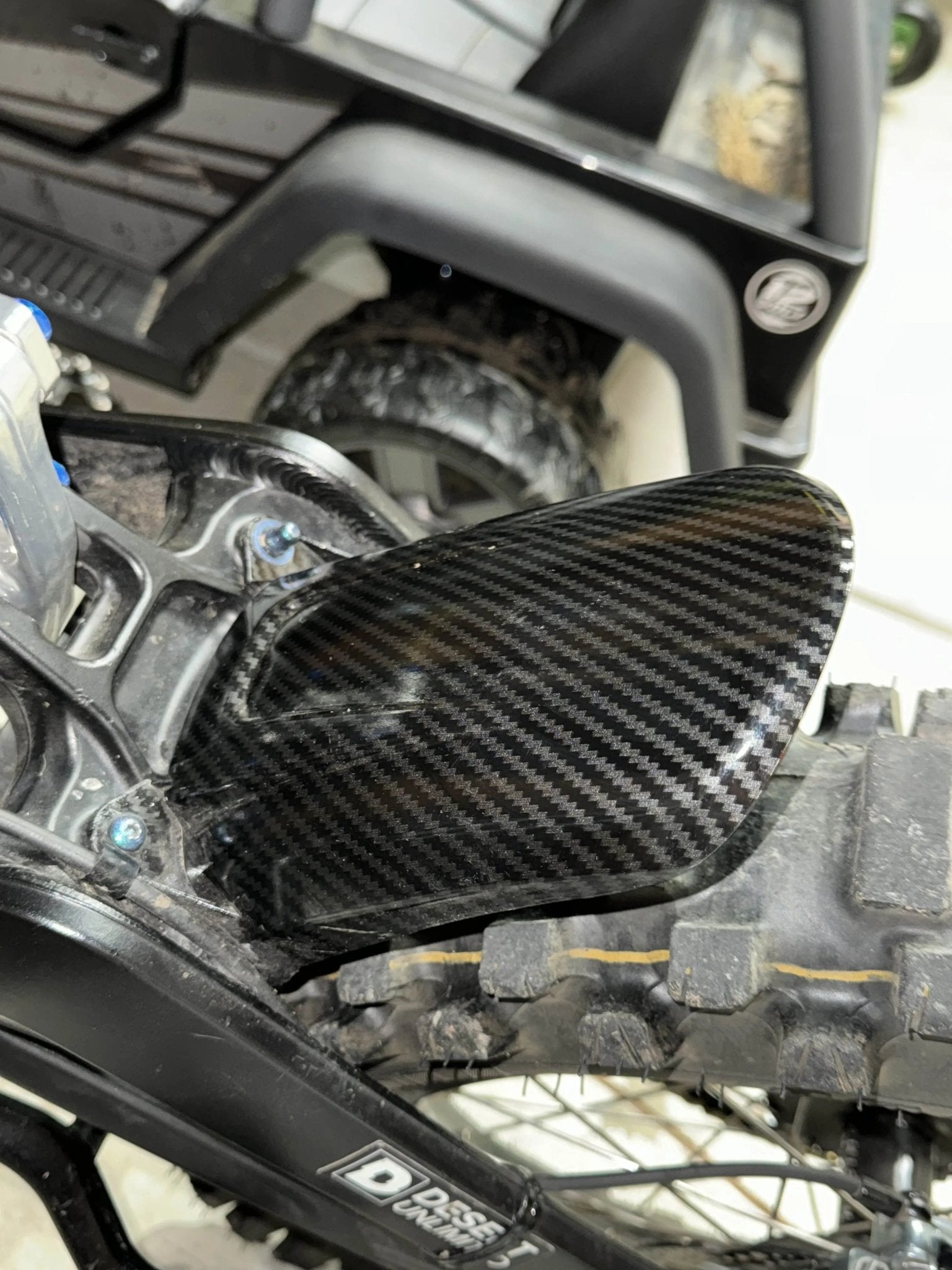 Rear wheel fender of a Surron LBX with MXwraps carbon fiber vinyl wrap kit, showcasing a sleek, textured carbon fiber finish.
